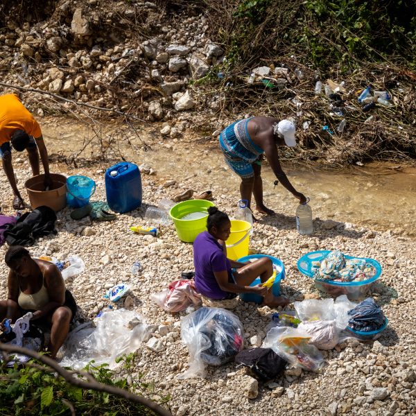 Without water, persons wash in streams of water brought by the hurricane